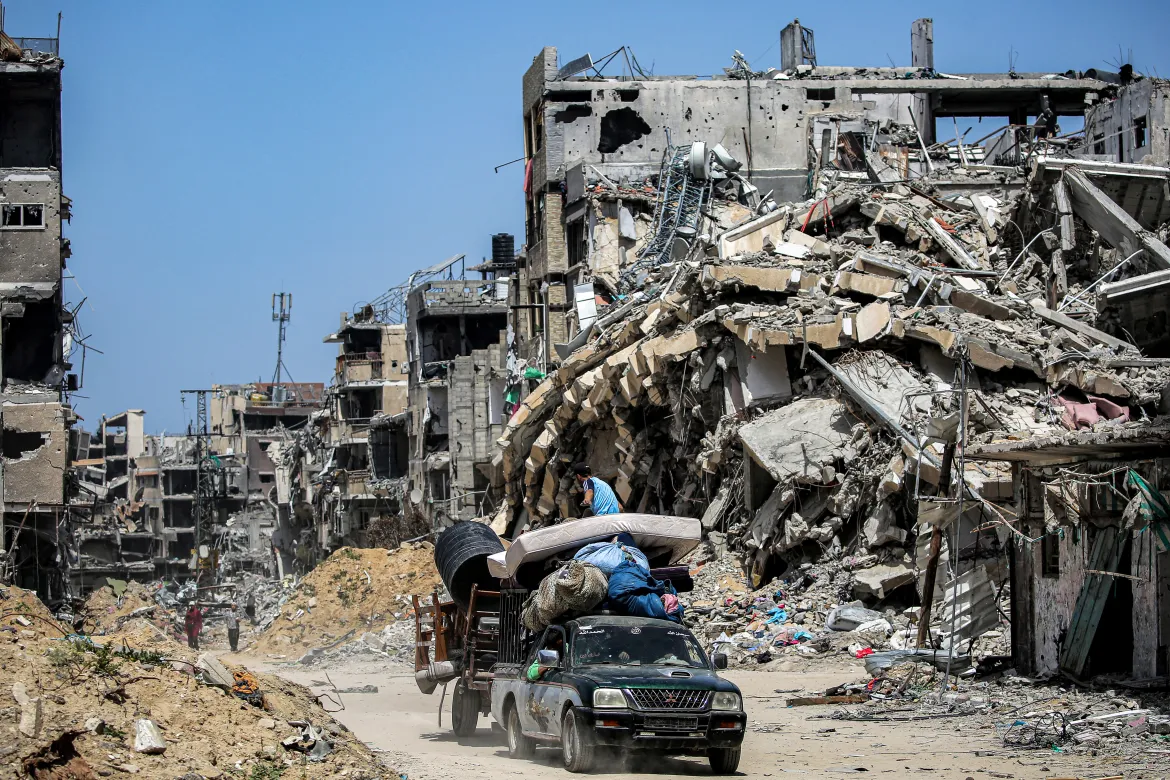 A pickup truck pulling a cart loaded with mattresses and furniture moves past destroyed buildings in Khan Younis in the southern Gaza Strip.