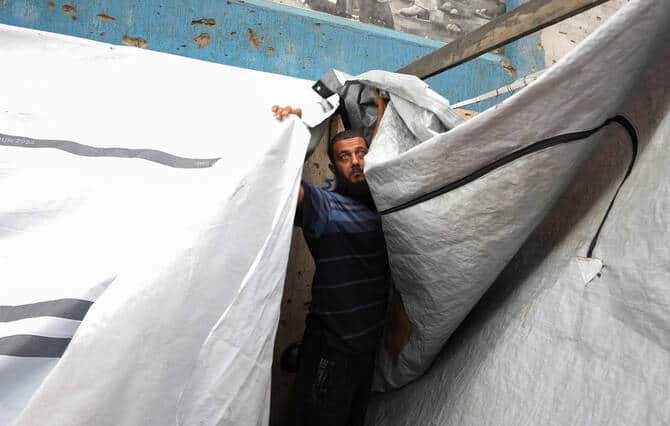 Man fixes a damaged tent in Gaza City during rain and a ceasefire.